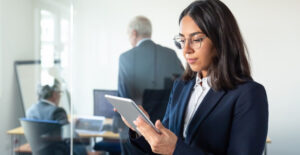 Revisão do cadastro de produtos — contadora com óculos consultando tablet em escritório corporativo