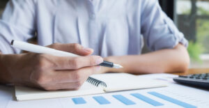 IBS e CBS tributos — contador anotando em caderno com gráficos de barras e calculadora sobre mesa