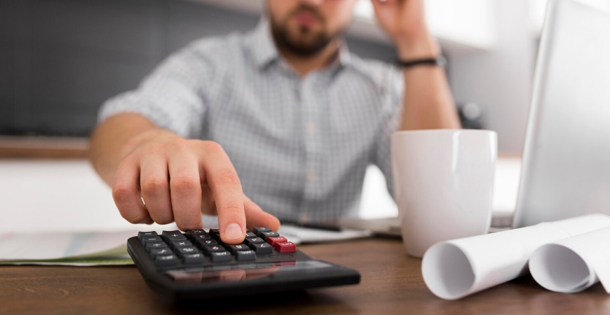 Planejamento tributário em tempos de transição — empresário usando calculadora com documentos e notebook sobre mesa