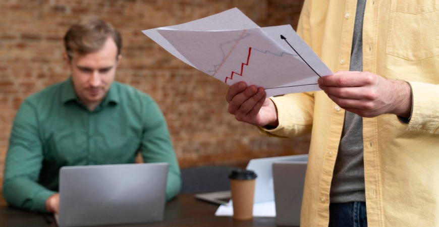 Imposto Seletivo quais produtos — empresário de camisa amarela analisando gráfico com linha de tendência em escritório