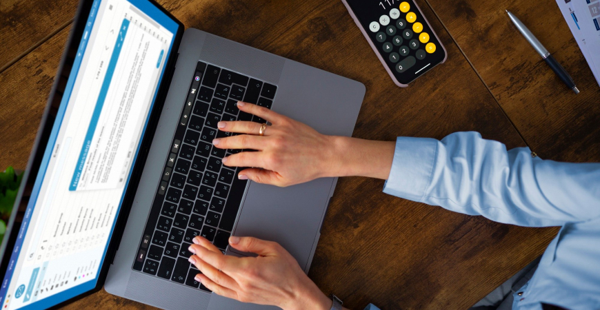 Split payment recolhimento automático — mãos de contadora digitando em notebook com calculadora ao lado sobre mesa de madeira